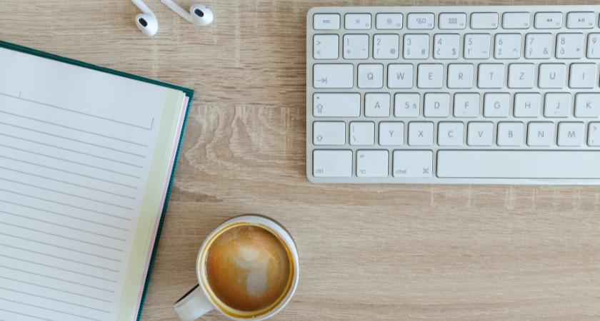 A notebook, coffee, earbuds and keyboard on a table